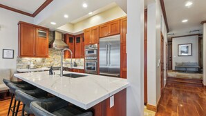 A modern kitchen with wooden cabinets, stainless steel appliances, and a marble island with bar stools.