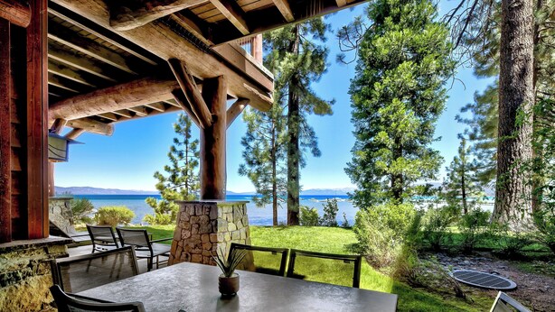 A patio with a table and chairs, overlooking a lake and surrounded by trees.