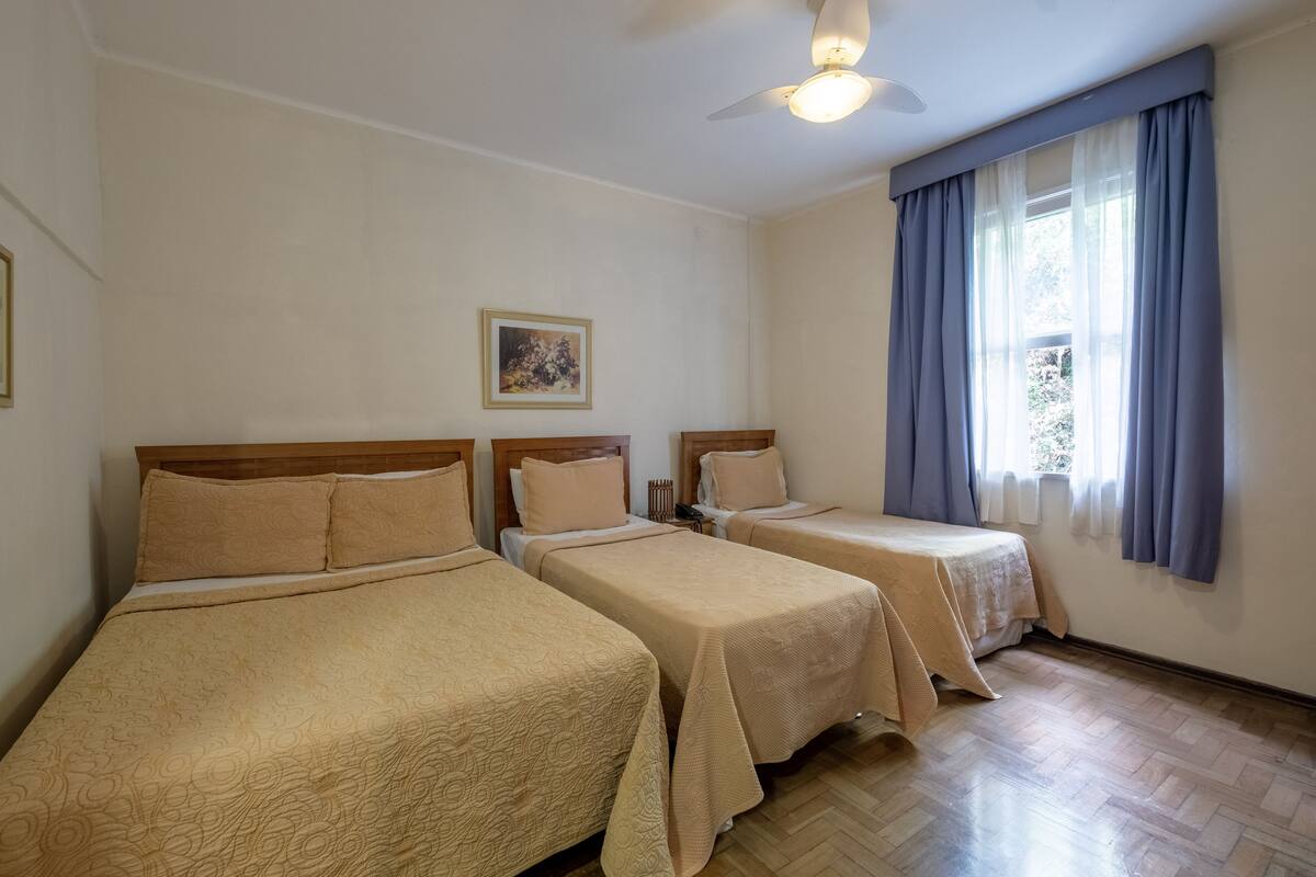 A hotel room with two single beds, a ceiling fan, a window with curtains, and a framed picture on the wall.