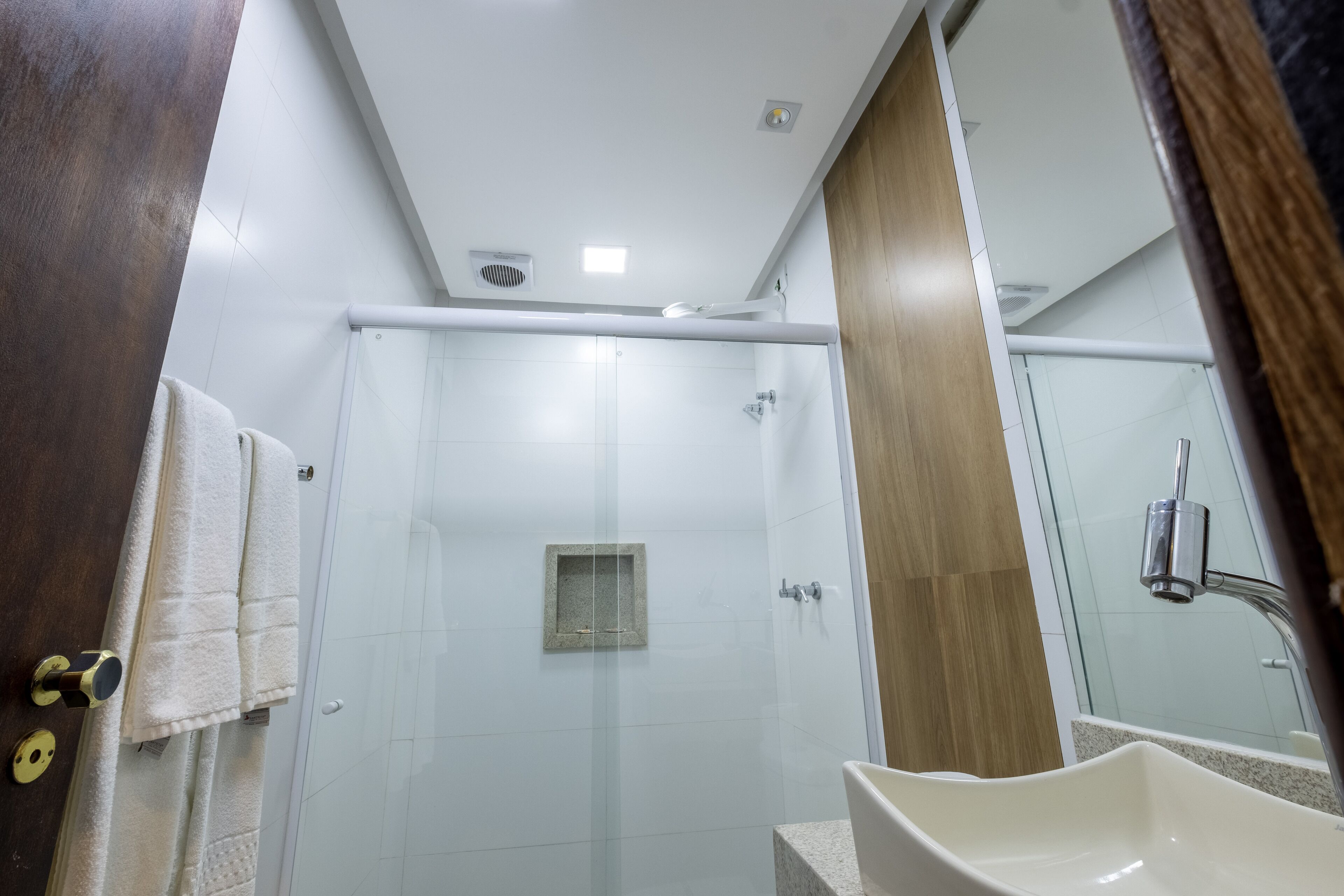Un baño moderno con cabina de ducha de vidrio, un lavabo blanco y un mueble de tocador de madera.