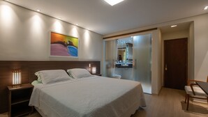 Een moderne hotelkamer met een groot bed, bedlampjes, een schilderij aan de muur en een zichtbare badkamer achter een glazen deur.