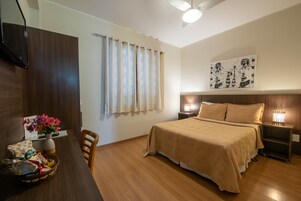 Un dormitorio con cama, mesitas de noche, un aparador, una ventana con cortinas, una obra de arte en la pared y suelo de madera.