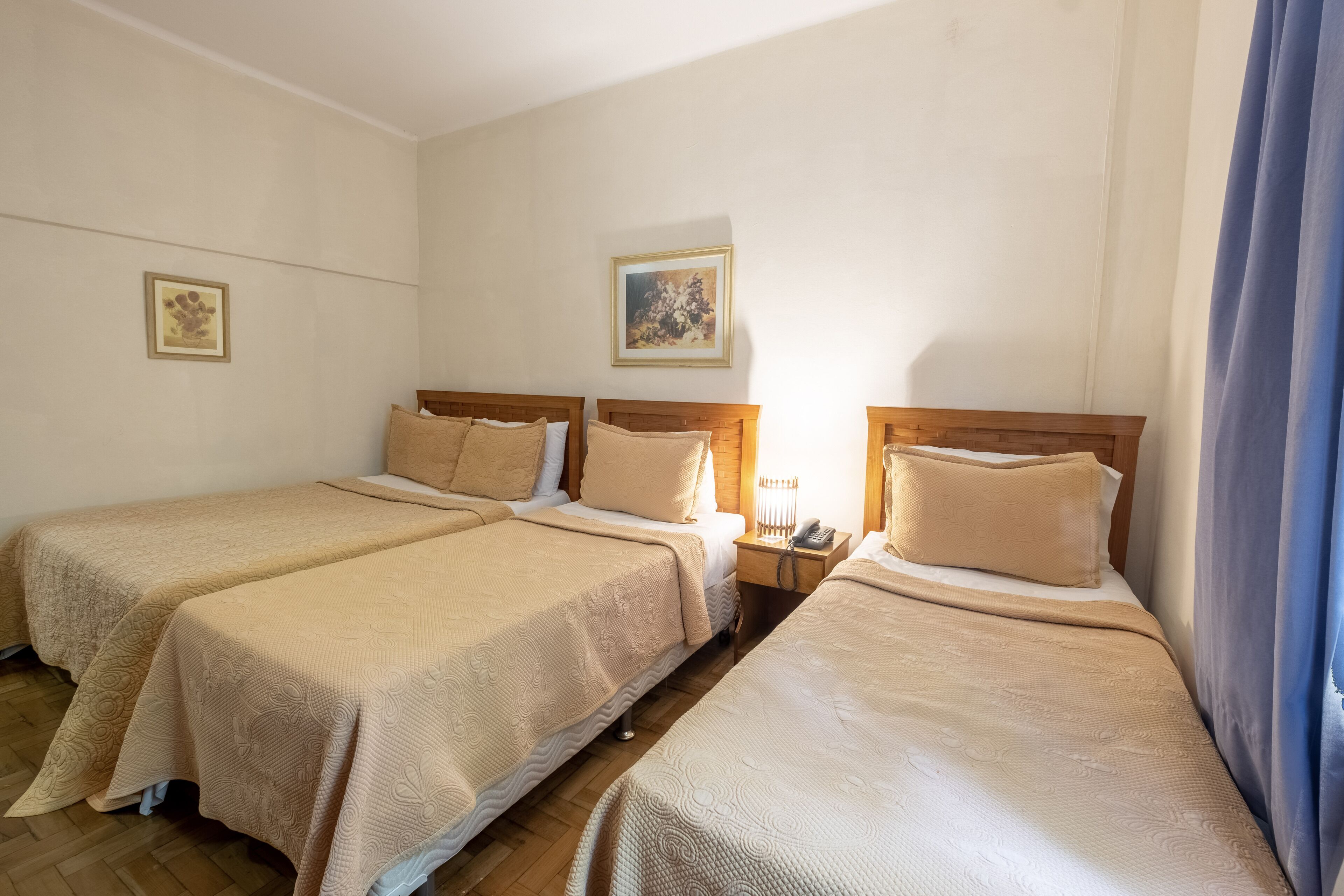 A hotel room with two single beds, a nightstand with a phone, and a painting on the wall.