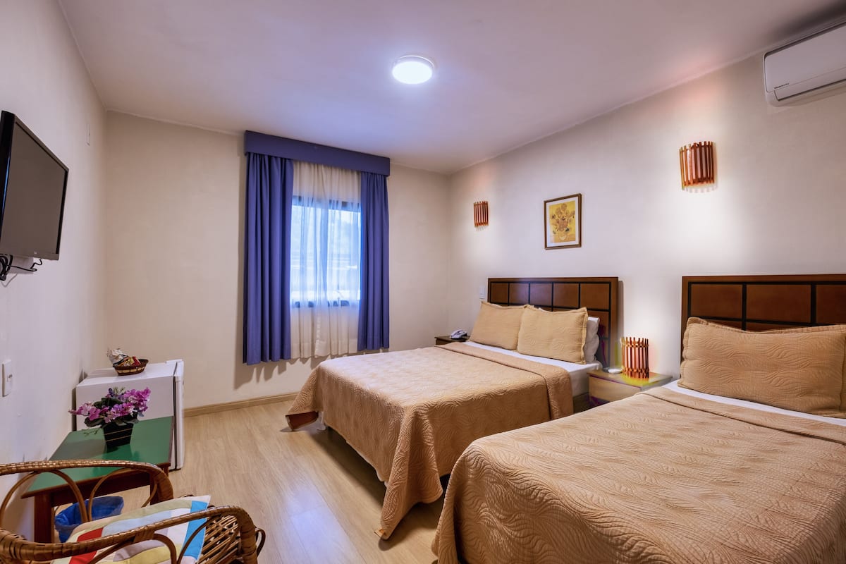 A hotel room with two beds, a television, a desk with a chair, and a window with curtains.