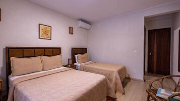 Quarto de hotel com duas camas, cabeceira de madeira, ar condicionado fixado na parede e um quadro emoldurado.
