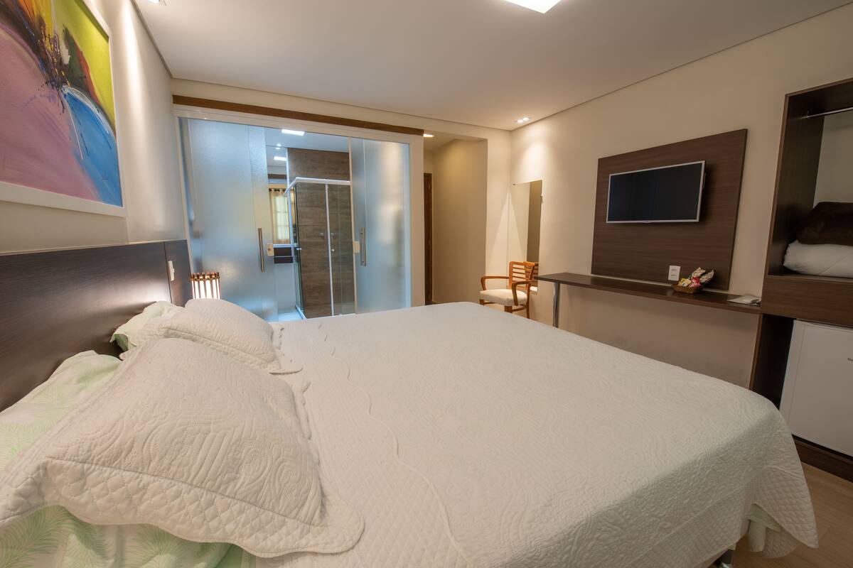 A modern hotel room with a large bed, a TV mounted on the wall, and a bathroom visible through an open door.