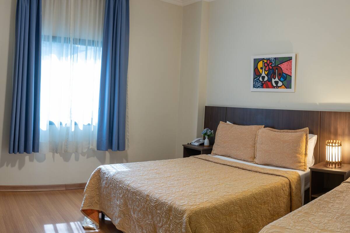 A hotel room with two beds, a desk, a TV, and two paintings on the wall.