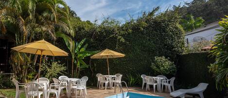 Una piscina con poltronne da relax bianche e ombrelloni, circondata dal verde e un cartello per un hotel.