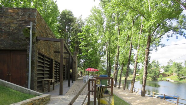 Un bâtiment en pierre doté d’une terrasse en bois et offrant une vue sur la rivière.