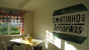 Un coin repas comprenant une table, des chaises et une fenêtre donnant sur un paysage verdoyant. Une décoration murale est visible.