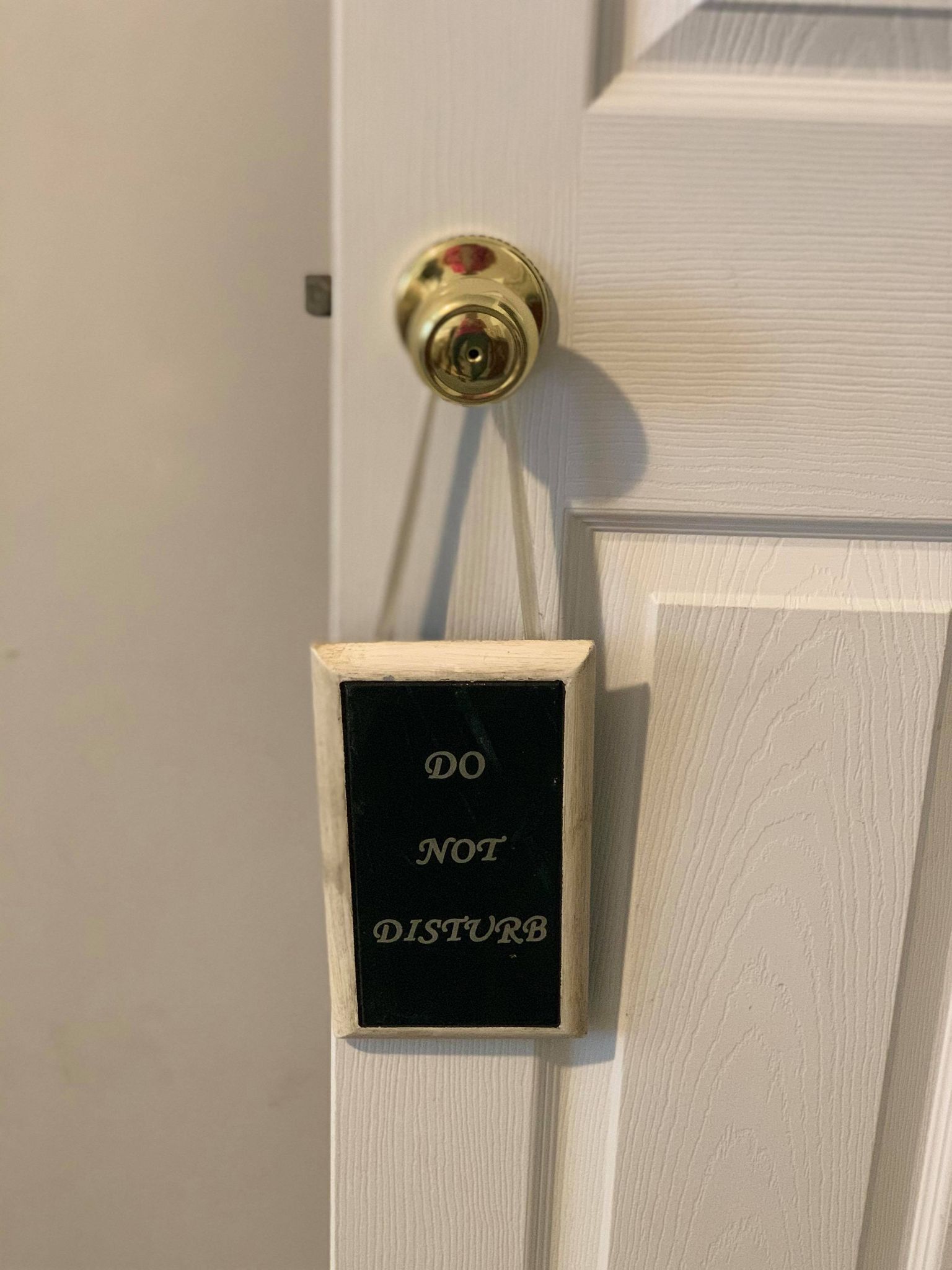 Eine Tür mit Messingklinke und einem kleinen, schwarzen Schild mit weißer Aufschrift: „DO NOT DISTURB“.
