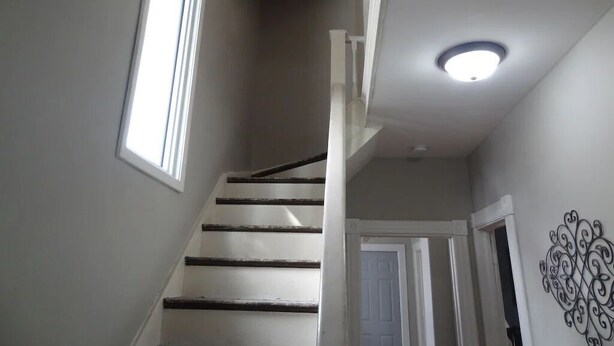 Una escalera con barandilla blanca, tragaluz y un adorno en la pared.