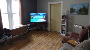 Una sala de estar con piso de madera, televisor, escritorio con silla, estantería y puerta.