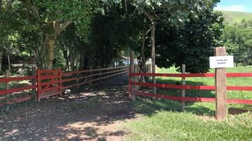 Una entrada con puerta adornada con un letrero que dice 'VIVENDA DOS GUARANYS', que da acceso a una zona verde exuberante con árboles y un cielo despejado.