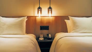 Habitación de hotel con dos camas, un cabecero de madera, una mesita de noche con teléfono y reloj, y dos lámparas colgantes.