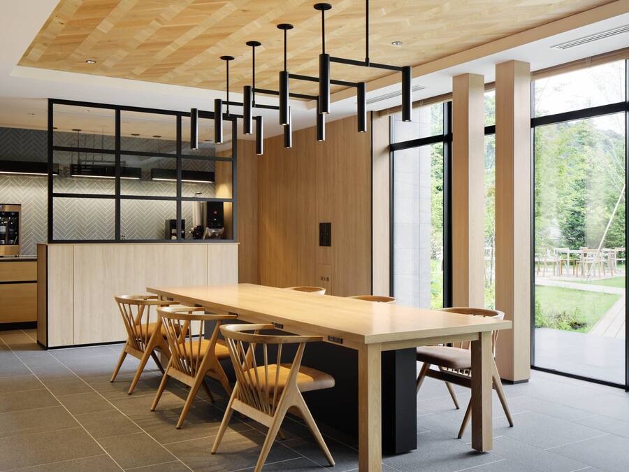 Une cuisine moderne avec une table et des chaises en bois, de grandes fenêtres et une vue sur l’extérieur.