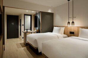 Habitación de hotel con dos camas, cabecero de madera, mesita de noche pequeña, un espejo y una lámpara colgante moderna.