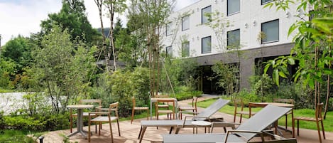 A modern outdoor patio with wooden furniture and a view of a white building with multiple windows.
