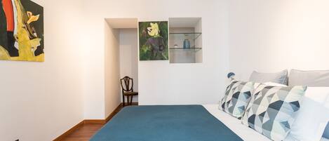 Un dormitorio moderno con una cama grande, una colcha azul y dos estantes empotrados con adornos decorativos.