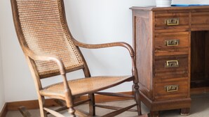 A wooden chair with a woven backrest and a wooden desk with drawers.