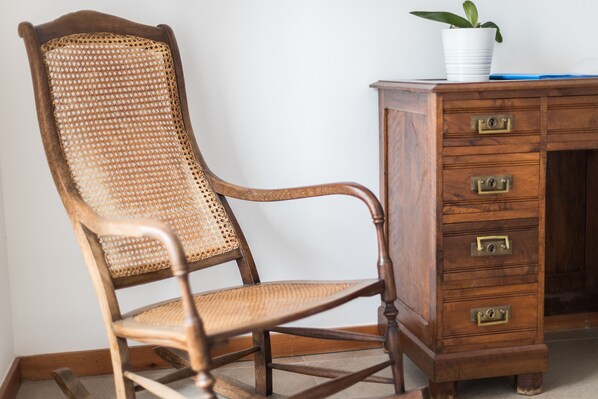 A wooden chair with a woven backrest and a wooden desk with drawers.