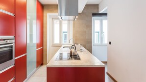 A modern kitchen with red cabinetry, a stainless steel kettle, and a built-in oven.