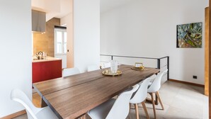 A modern dining area with a wooden table, white chairs, and a kitchen in the background.
