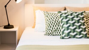 A neatly made bed with white and green patterned pillows, a black desk lamp, and a glass shelf above the bed.