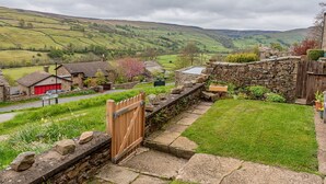 Paisaje rural con casas de piedra, un muro de piedra y una puerta de madera.