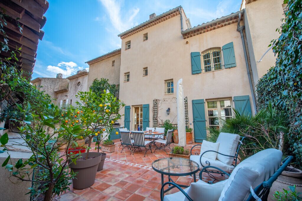 A courtyard with a table and chairs, surrounded by buildings with shutters.