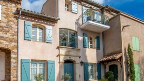 Un bâtiment à deux étages doté d’une façade en pierre, de nombreuses fenêtres avec volets et d’un balcon.