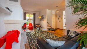 Un salon moderne avec un canapé en cuir noir, une table basse en verre et un fauteuil rouge. Un escalier mène à un autre niveau, et une grande plante est visible dans un coin.