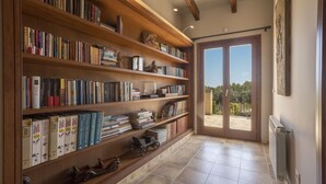 Ein geräumiges Zimmer mit einem großen Bücherregal voller Bücher, einem Heizkörper und Blick durch eine Glastür auf einen Außenbereich.