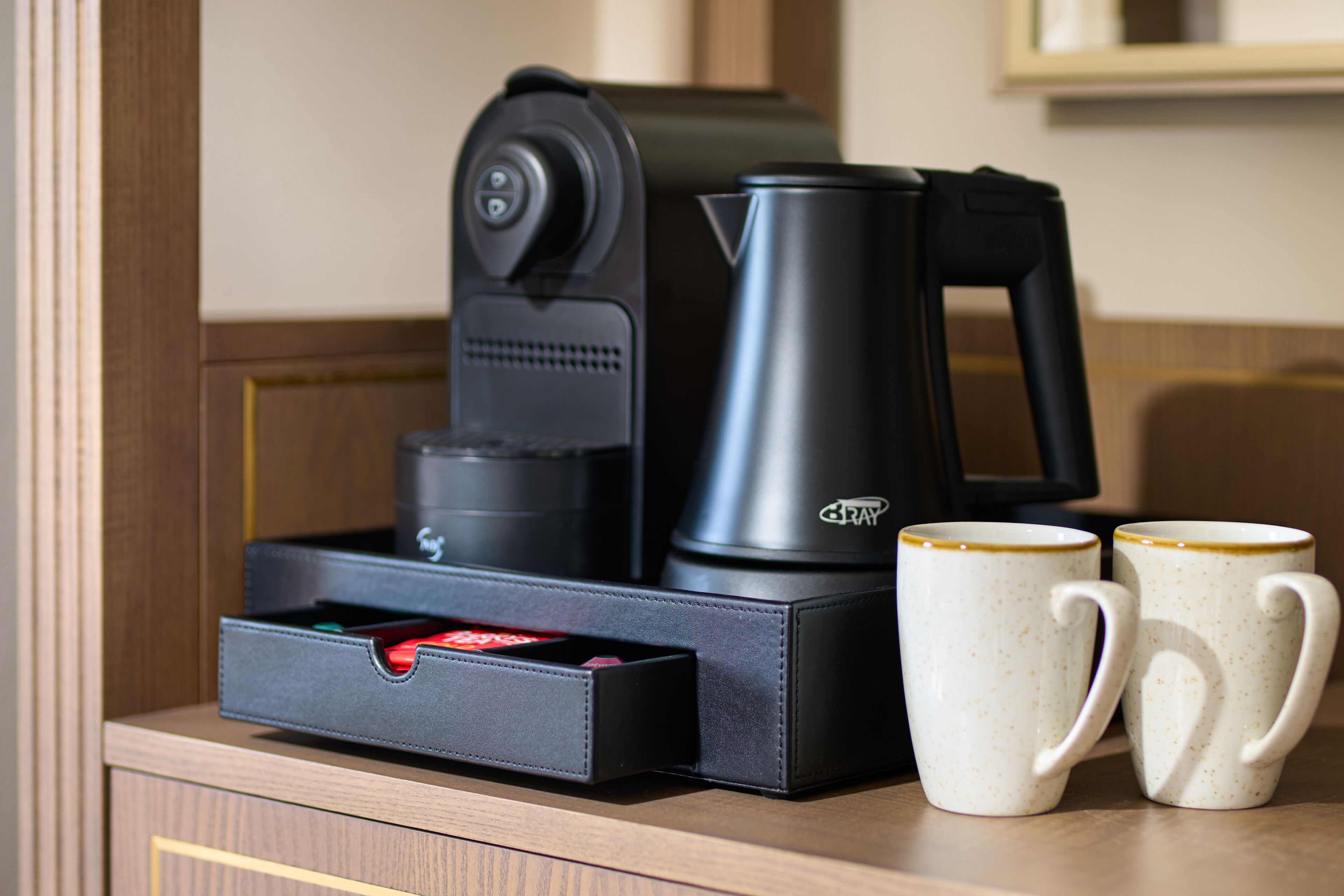 A coffee maker, a kettle, and two mugs on a wooden surface.