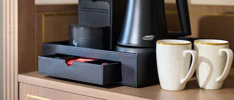 A coffee maker, a kettle, and two mugs on a wooden surface.