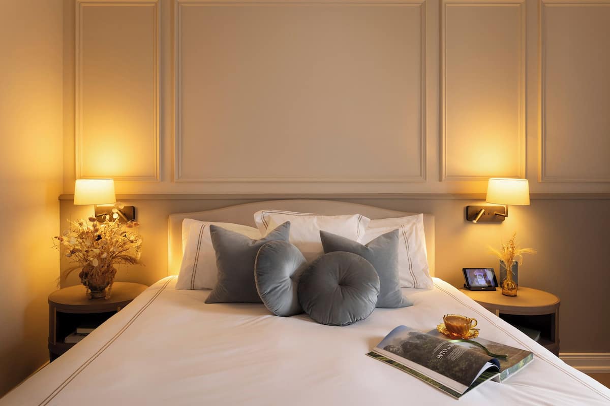 A neatly made bed with pillows, a magazine, and a cup on a bedside table.