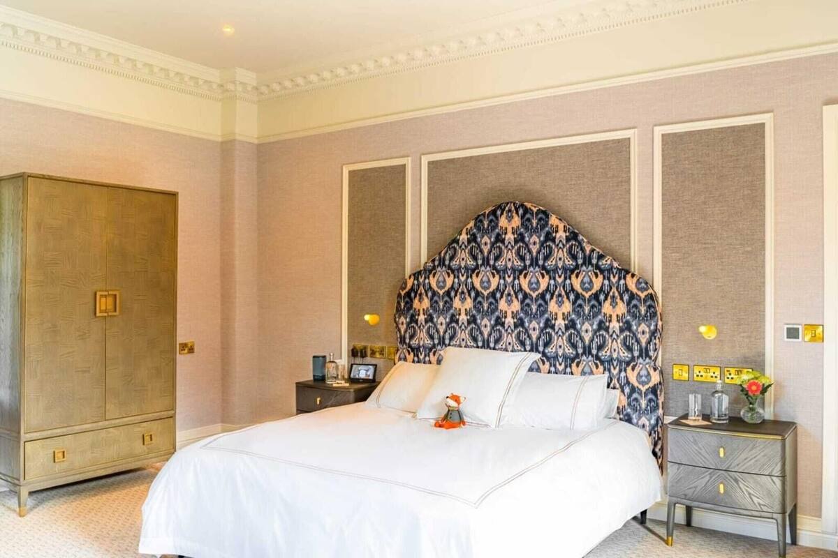 A hotel room with a large bed, a wardrobe, a nightstand with a lamp, and a decorative headboard.