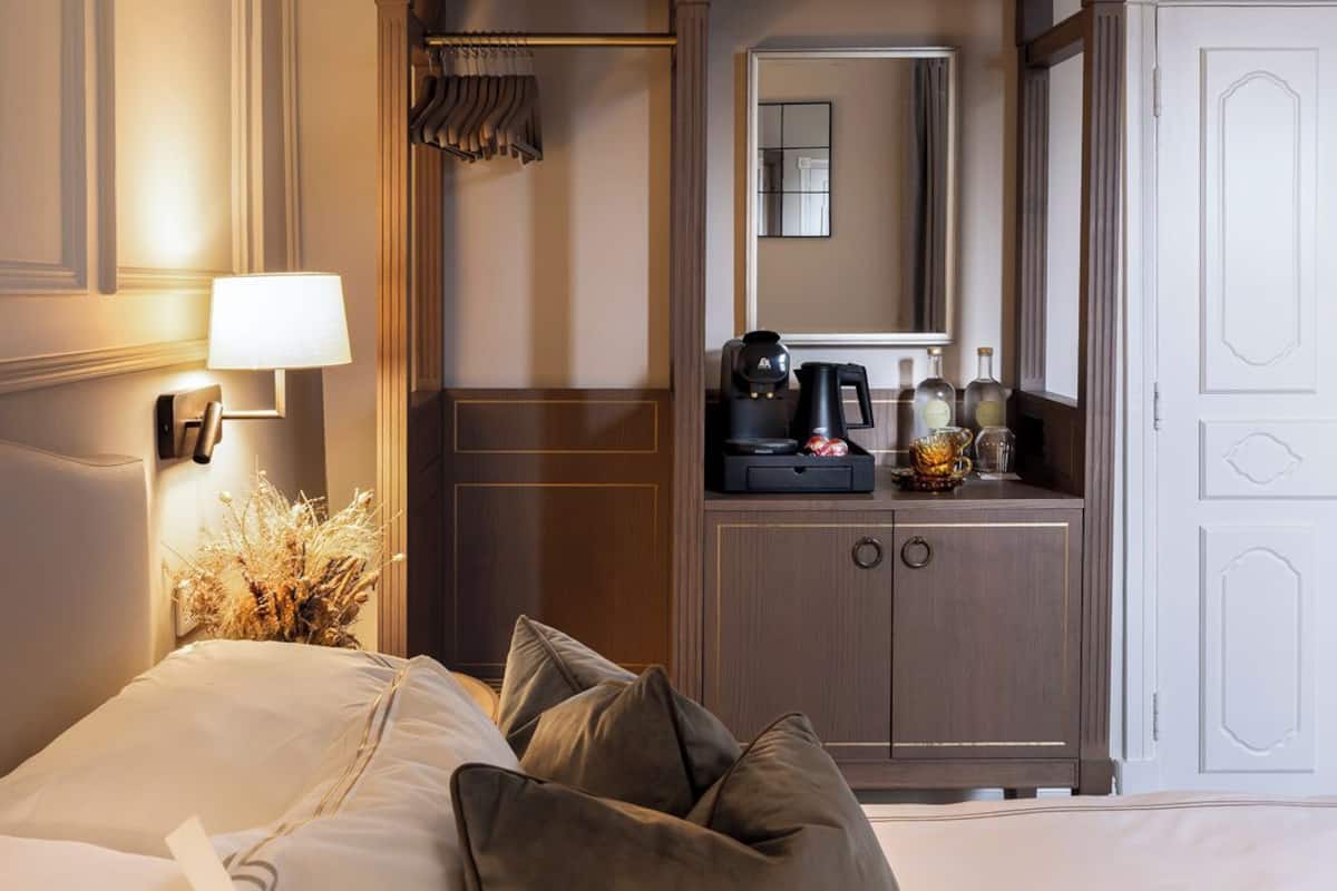 A hotel room with a bed, a nightstand with a lamp, a dresser with a mirror, and a coffee maker.