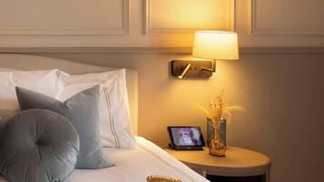 A neatly made bed with pillows, a bedside table with a lamp, a tablet, a vase with dried plants, and a magazine.