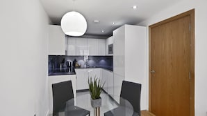 A modern kitchen with white cabinets, a black countertop, and a glass dining table with two chairs.