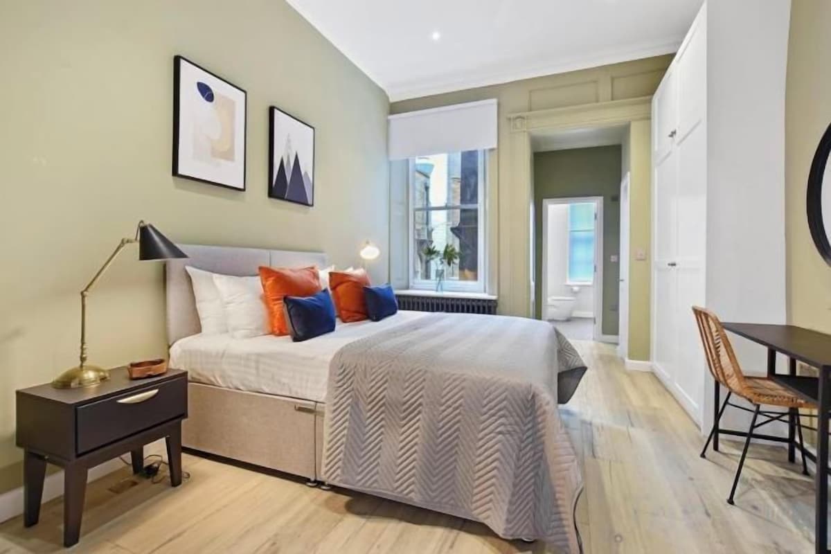 Un dormitorio con cama, mesita de noche, lámpara y una silla.