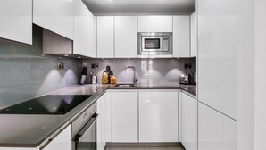 A modern kitchen with white cabinetry, a built-in microwave, a stainless steel sink, and a black countertop.