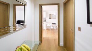 A hallway with a fruit bowl, wooden flooring, and a dining area with white chairs and a table.