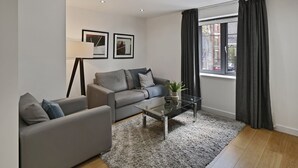 A modern living room with a grey sofa, a glass coffee table, and a large window with curtains.