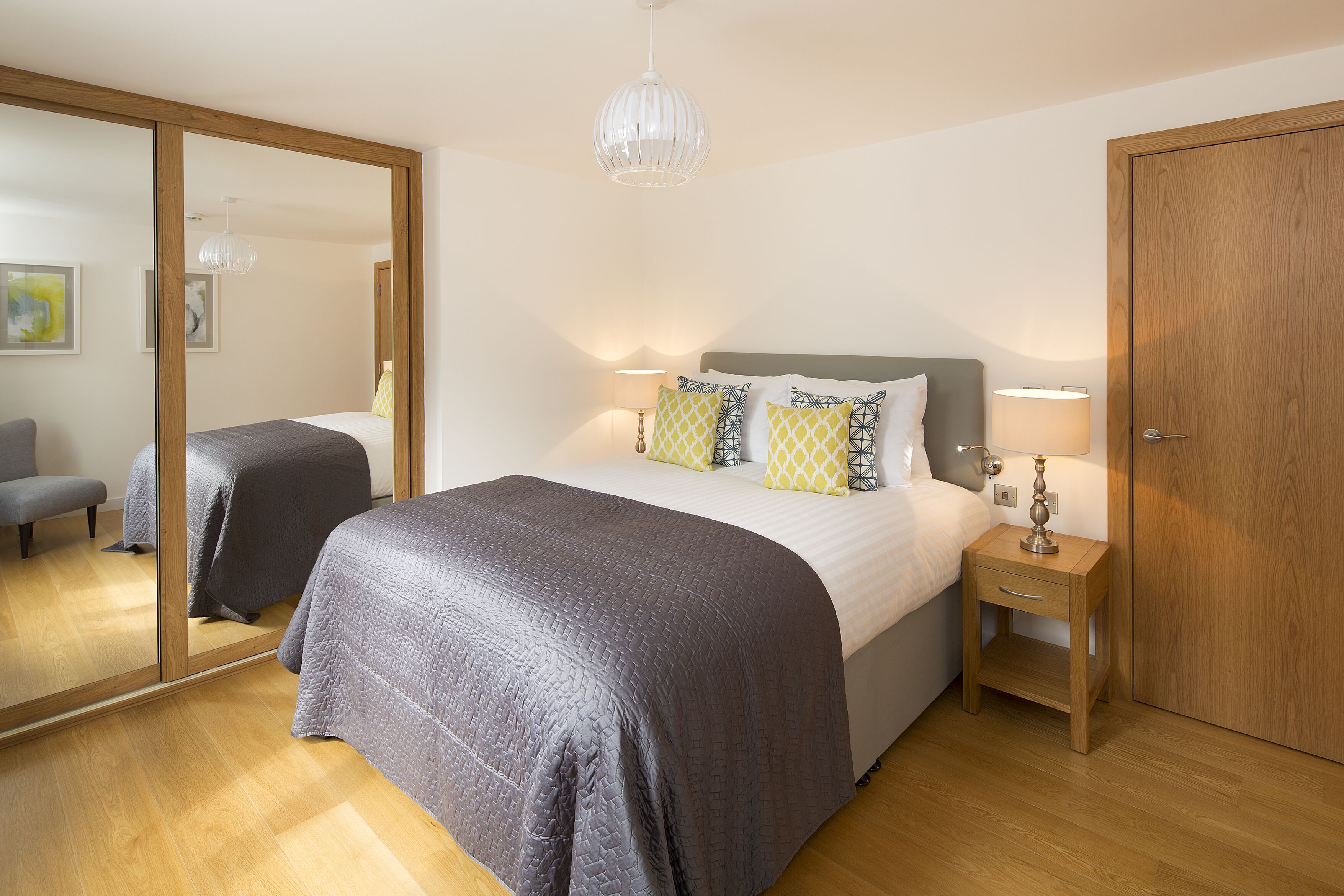 Ein Schlafzimmer mit einem großen Bett, Nachttischen, einem Spiegel und Holzboden.