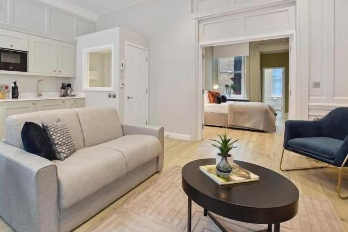 A modern living room with a sofa, a coffee table, and a kitchen area with white cabinets and appliances.