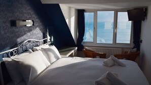 A hotel room with a bed, a window with a view of the sea, a television, and a chair. - Penn House Hotel (Weymouth)