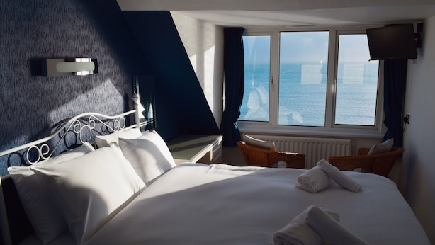 A hotel room with a bed, a window with a view of the sea, a television, and a chair.
