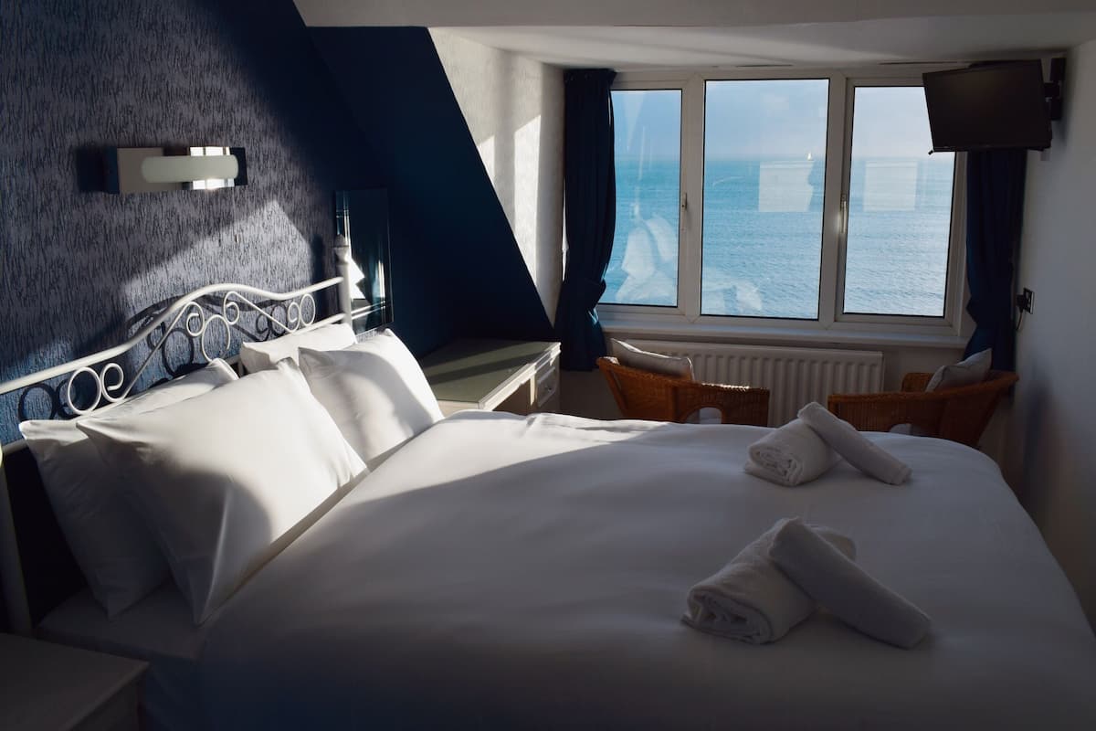 A hotel room with a bed, a window with a view of the sea, a television, and a chair.