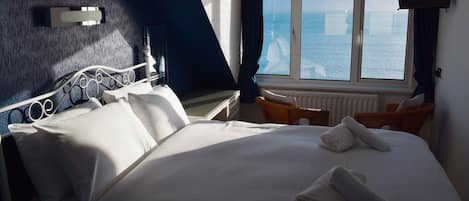 Habitación de hotel con cama, ventana con vista al mar, televisión y una silla.